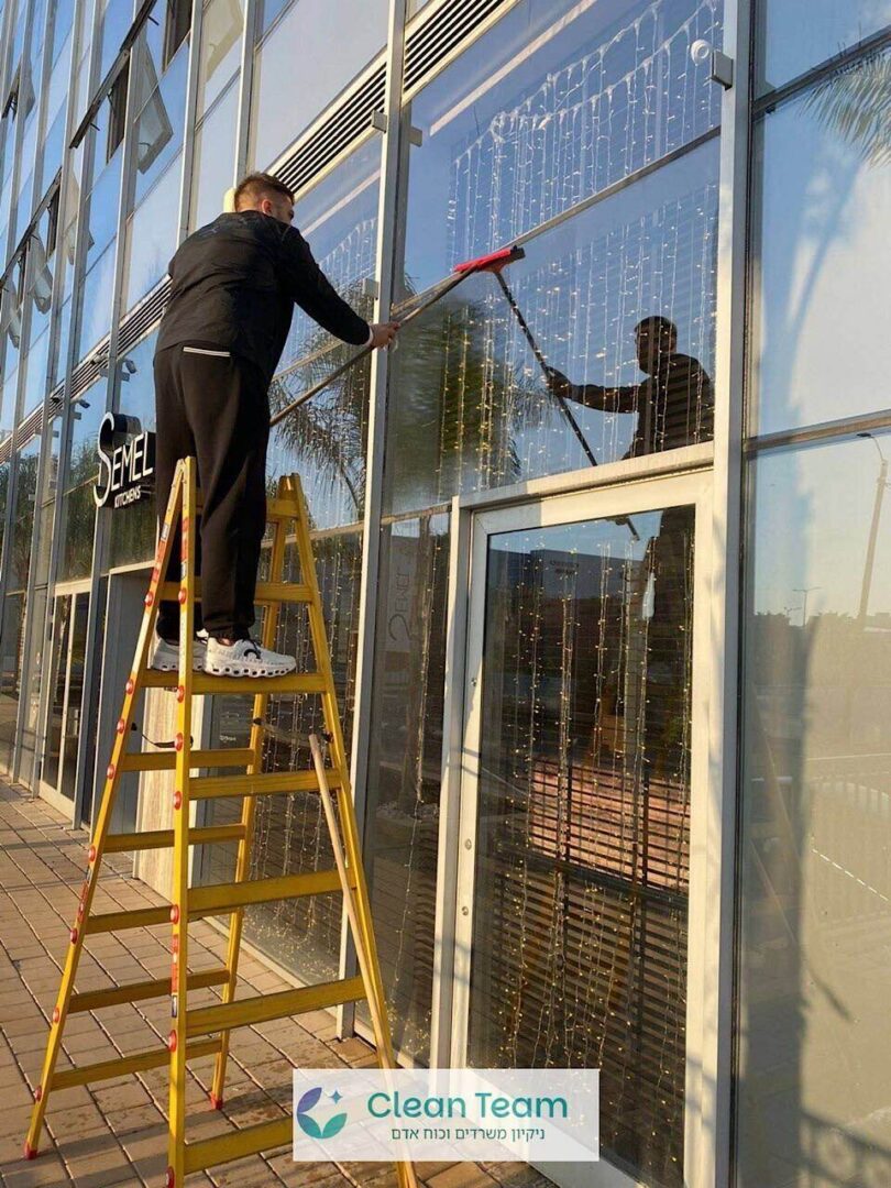 עובד Clean Team מנקה חלונות בגובה מסולם