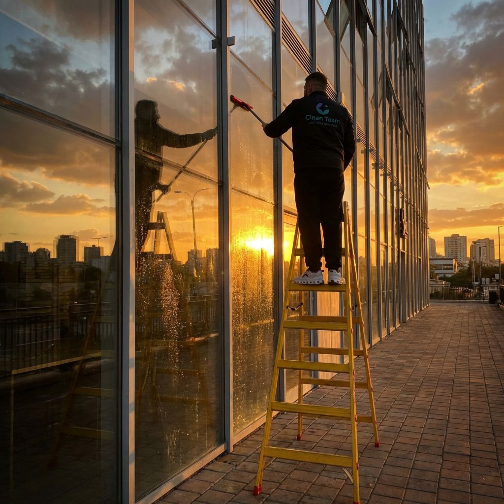 עובד Clean Team מנקה חלונות בגובה על סולם בבניין משרדים